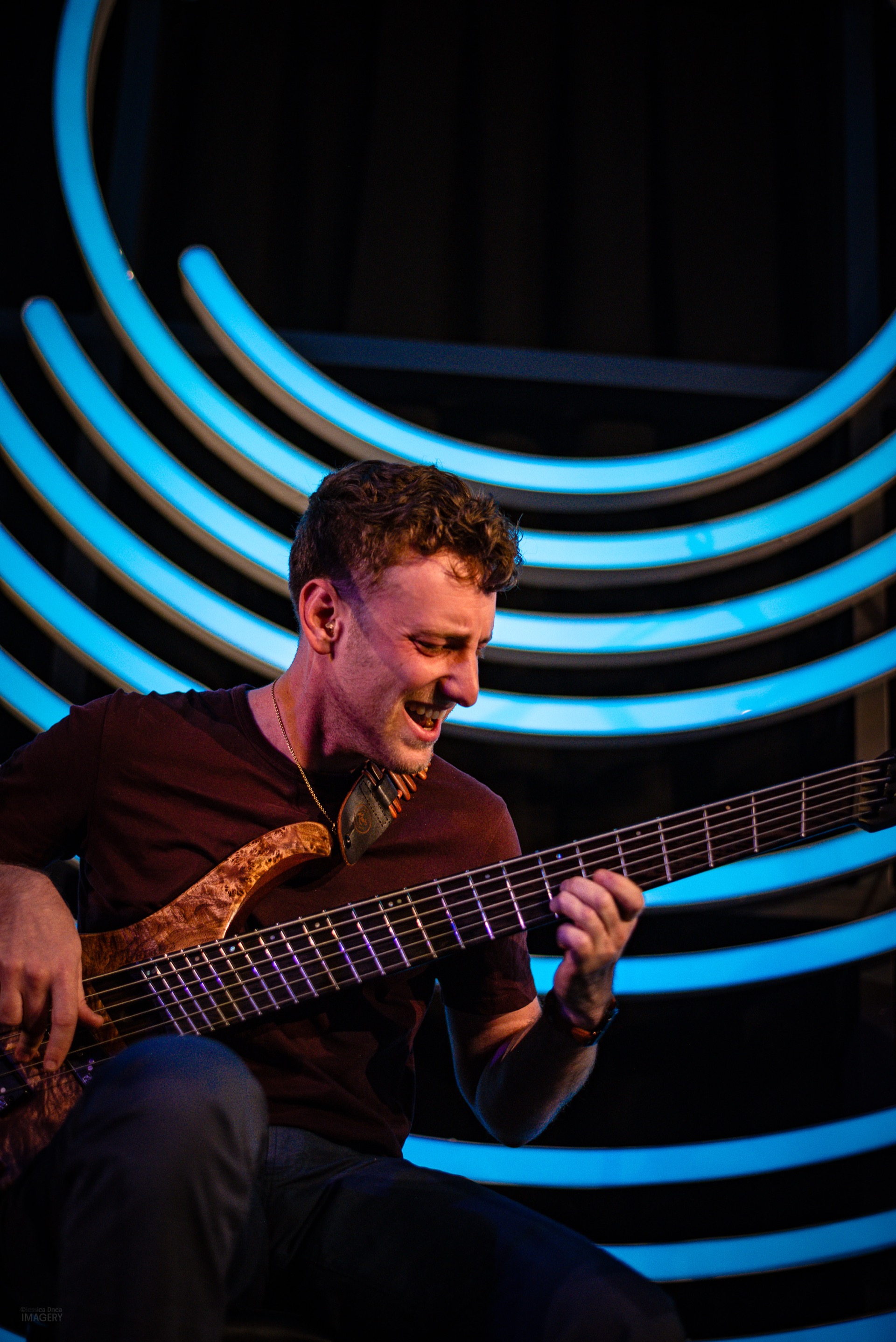 Jordan Lovinger laughing while playing six-string bass under the Dazzle neon rings
