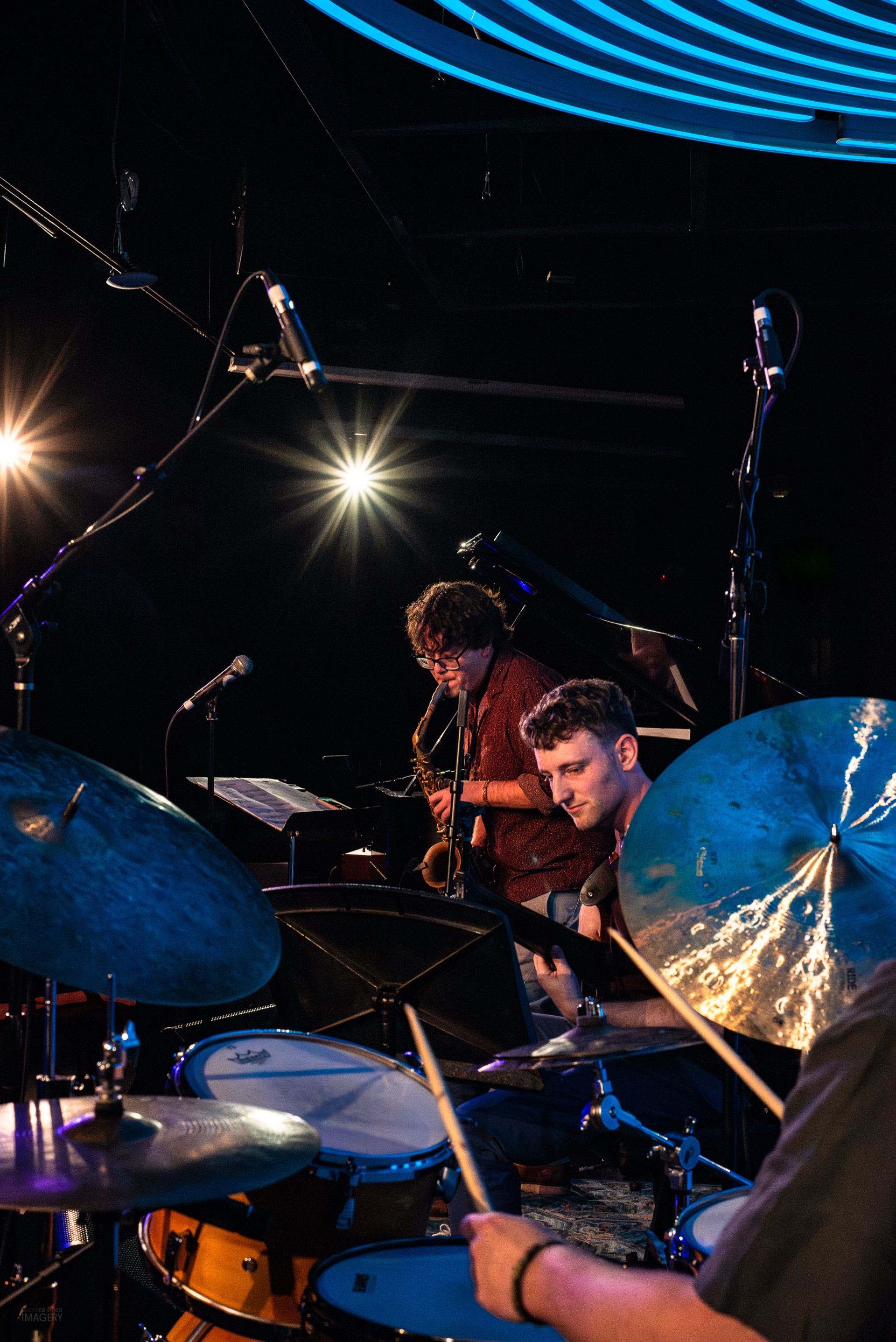 Chick Magnet trio with drums and saxophone under the Dazzle neon rings